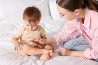 Photo of Mother applying cream onto her baby's leg on bed at home