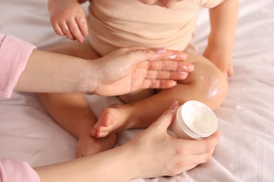 Photo of Mother applying cream onto her baby's leg on bed at home, closeup