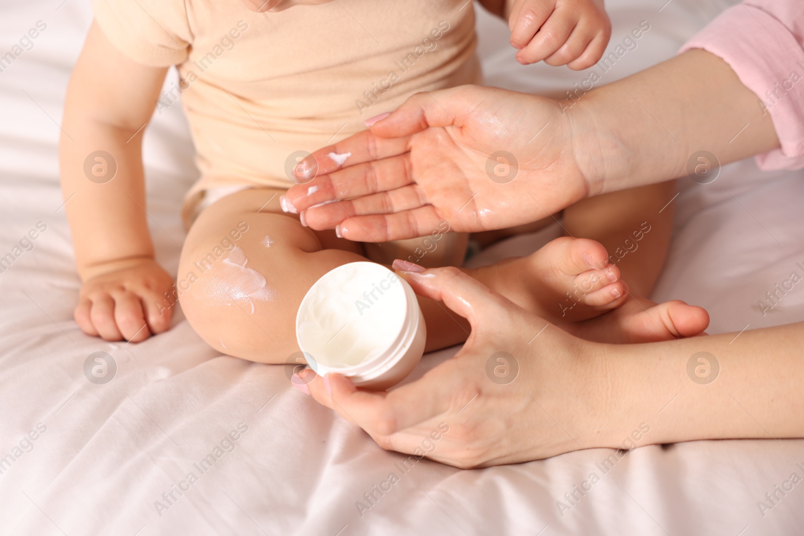 Photo of Mother applying cream onto her baby's leg on bed at home, closeup