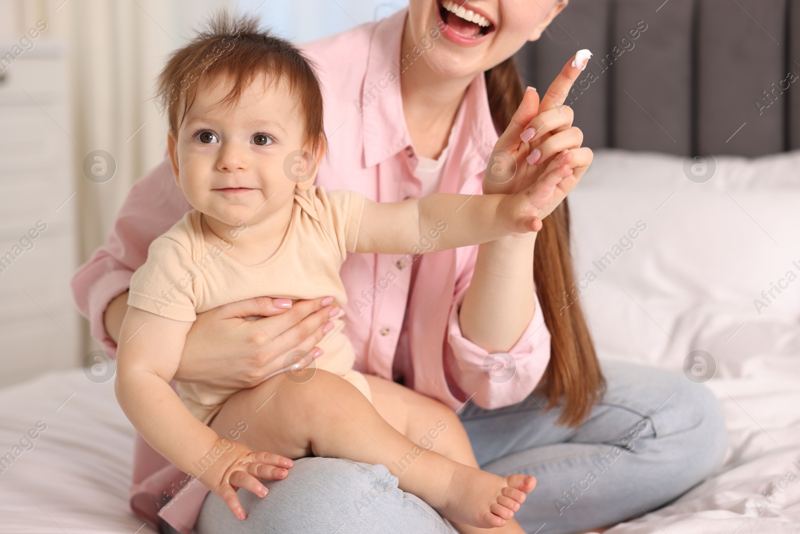 Photo of Mother applying cream onto her baby's body on bed at home