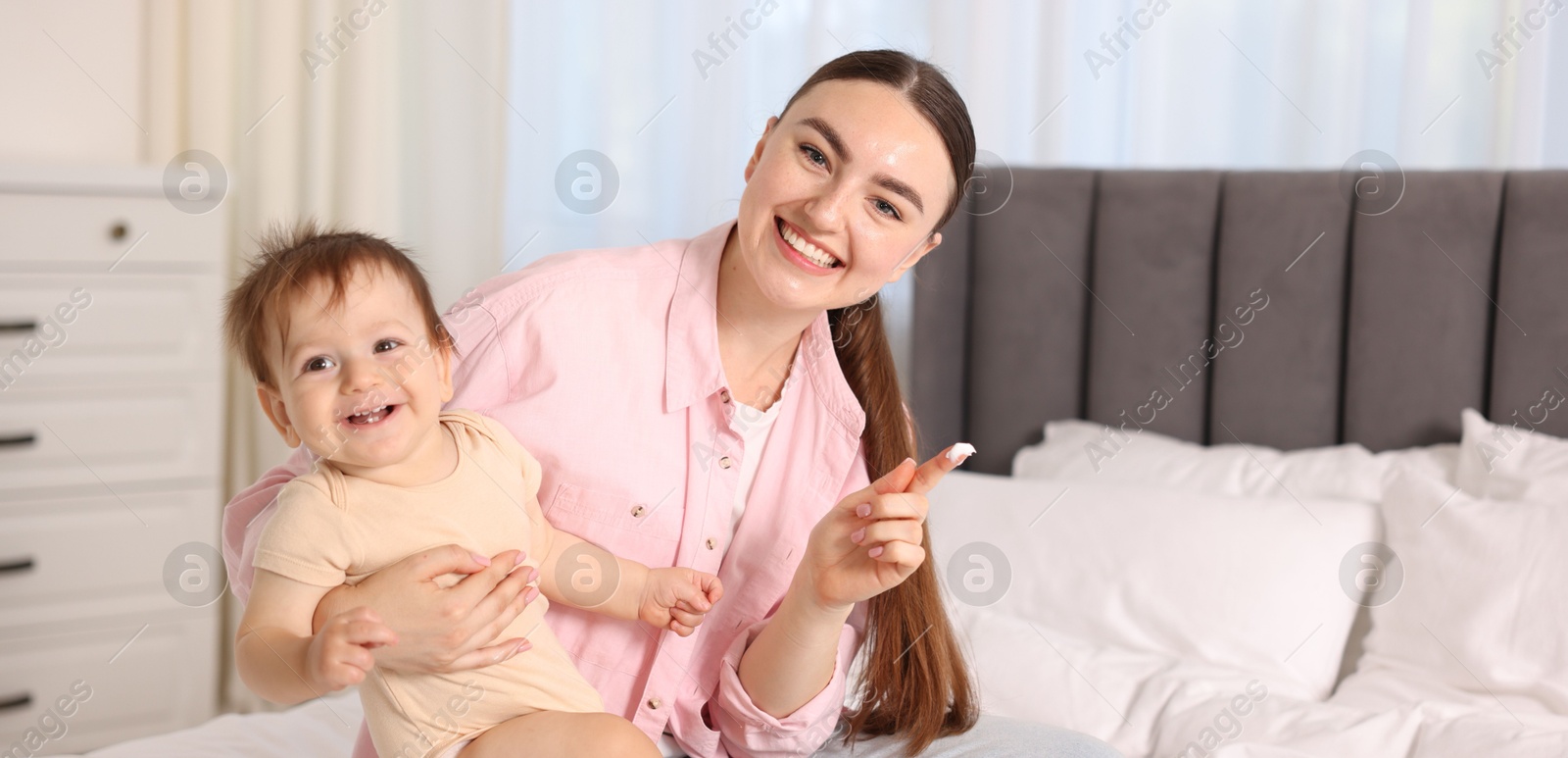 Photo of Mother applying cream onto her baby's body on bed at home