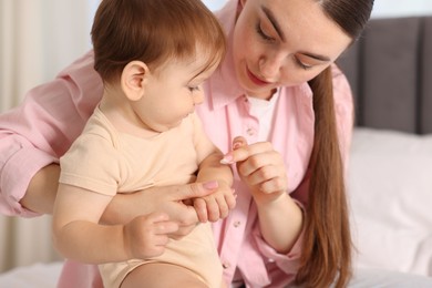 Photo of Mother applying cream onto her baby's arm on bed at home, closeup
