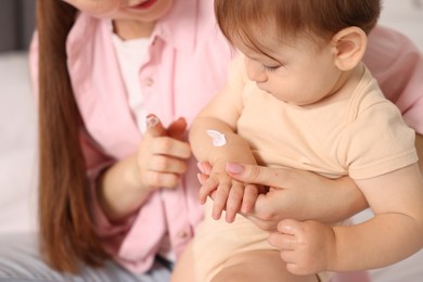 Photo of Mother applying cream onto her baby's arm on bed at home, closeup
