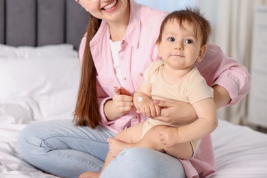 Photo of Mother applying cream onto her baby's arm on bed at home, closeup