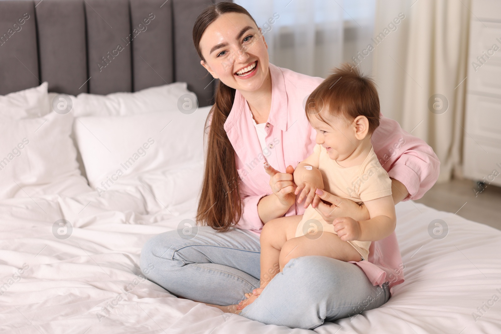 Photo of Mother applying cream onto her baby's arm on bed at home