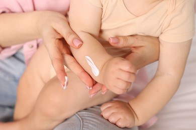 Photo of Mother applying cream onto her baby's arm on bed at home, closeup