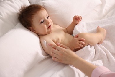 Photo of Mother applying cream onto her baby's body on bed at home, closeup