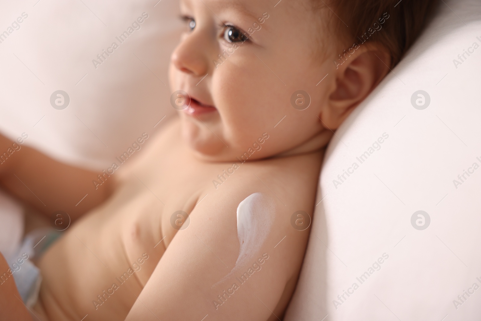 Photo of Cute little baby with cream on his body lying in bed, closeup