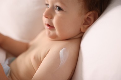 Photo of Cute little baby with cream on his body lying in bed, closeup