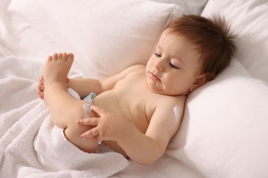 Photo of Cute little baby with cream on his body lying in bed