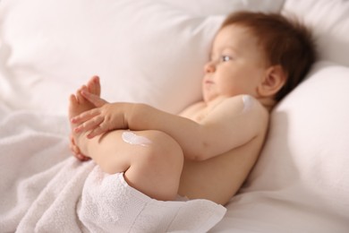 Photo of Cute little baby with cream on his body lying in bed