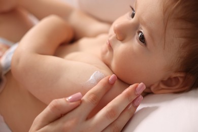 Photo of Mother applying cream onto her baby's body on bed at home, closeup