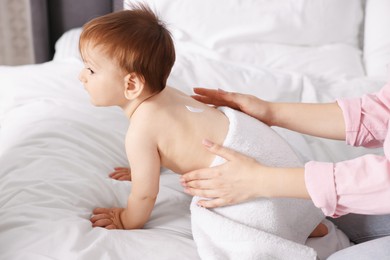 Photo of Mother applying cream onto her baby's back on bed at home, closeup