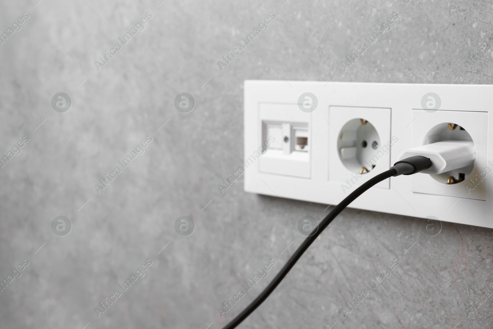 Photo of USB adapter with cable plugged into electric socket on grey wall, closeup. Space for text