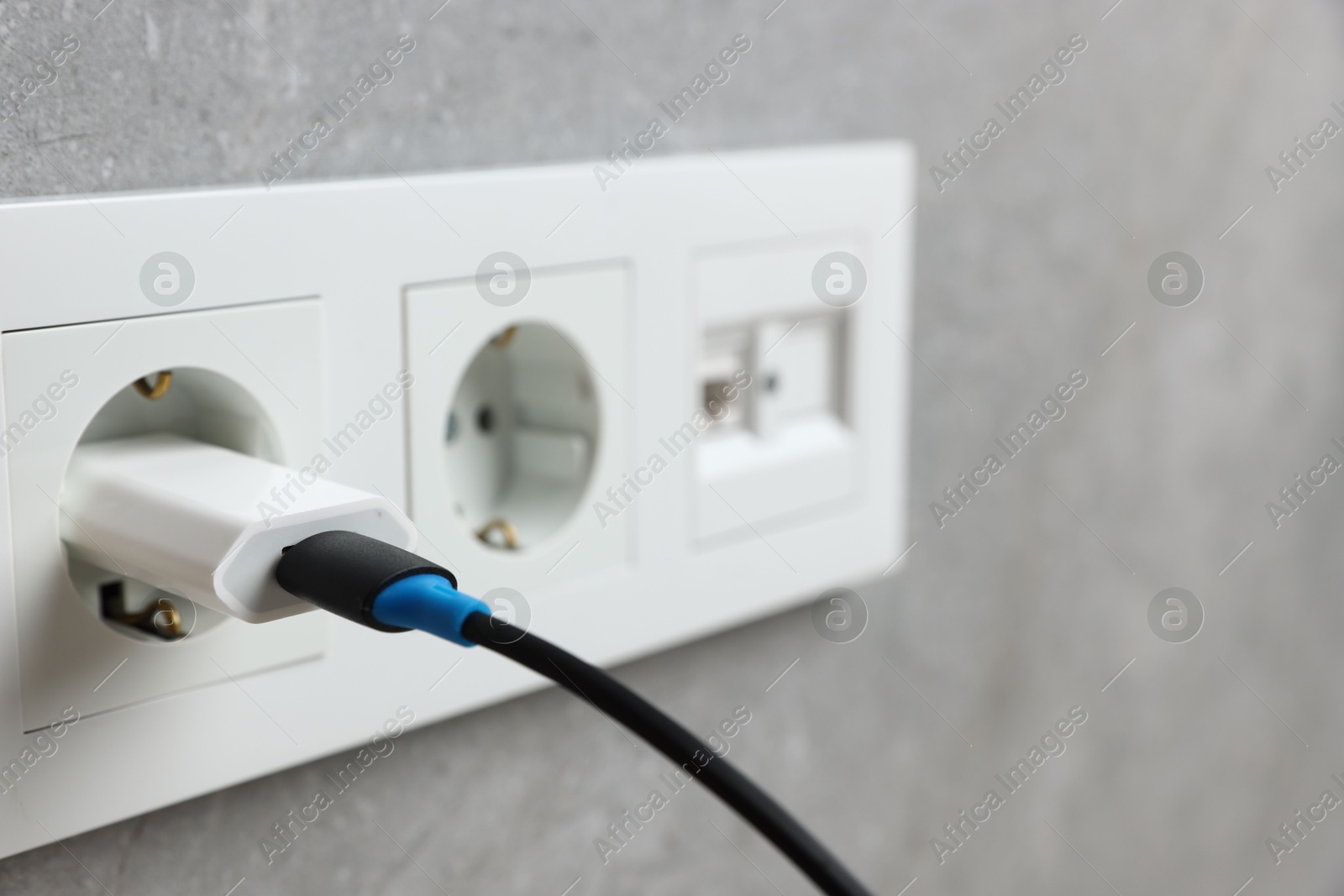 Photo of USB adapter with cable plugged into electric socket on grey wall, closeup. Space for text