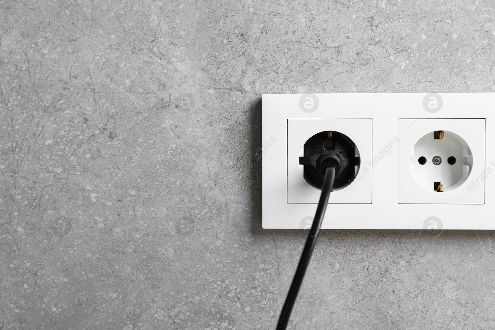 Photo of Power plug in socket on grey wall, closeup. Space for text