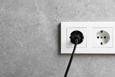 Photo of Power plug in socket on grey wall, closeup. Space for text