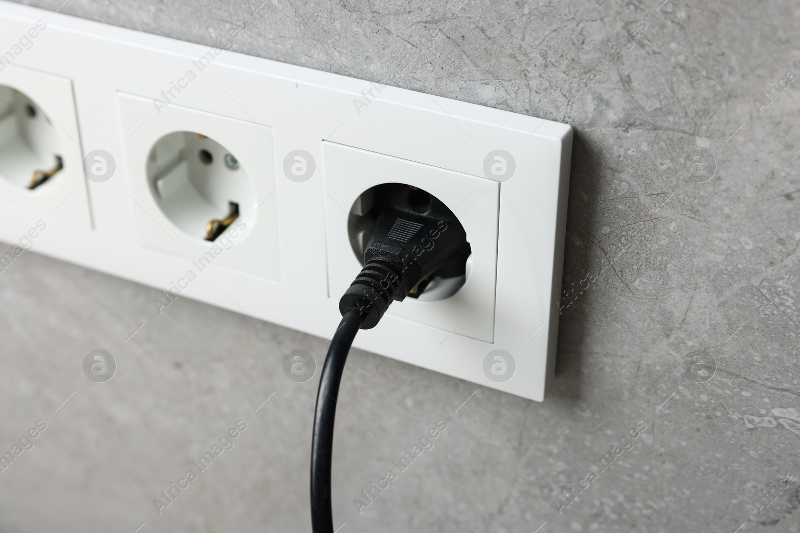 Photo of Power plug in socket on grey wall, closeup