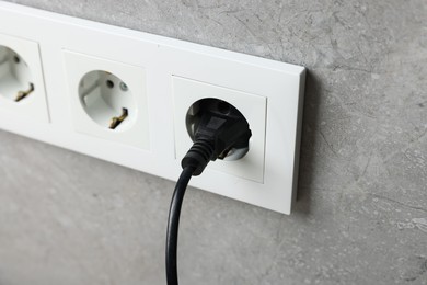 Photo of Power plug in socket on grey wall, closeup