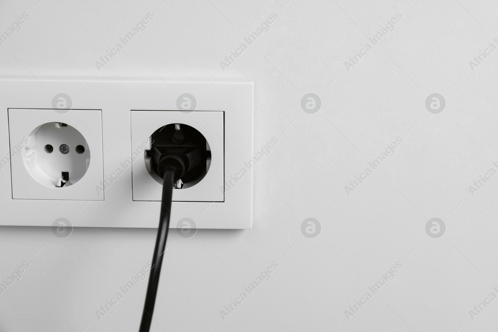 Photo of Power plug in socket on white wall, closeup. Space for text