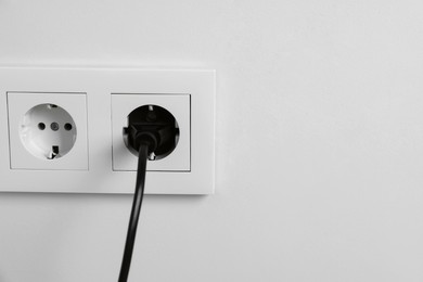 Photo of Power plug in socket on white wall, closeup. Space for text