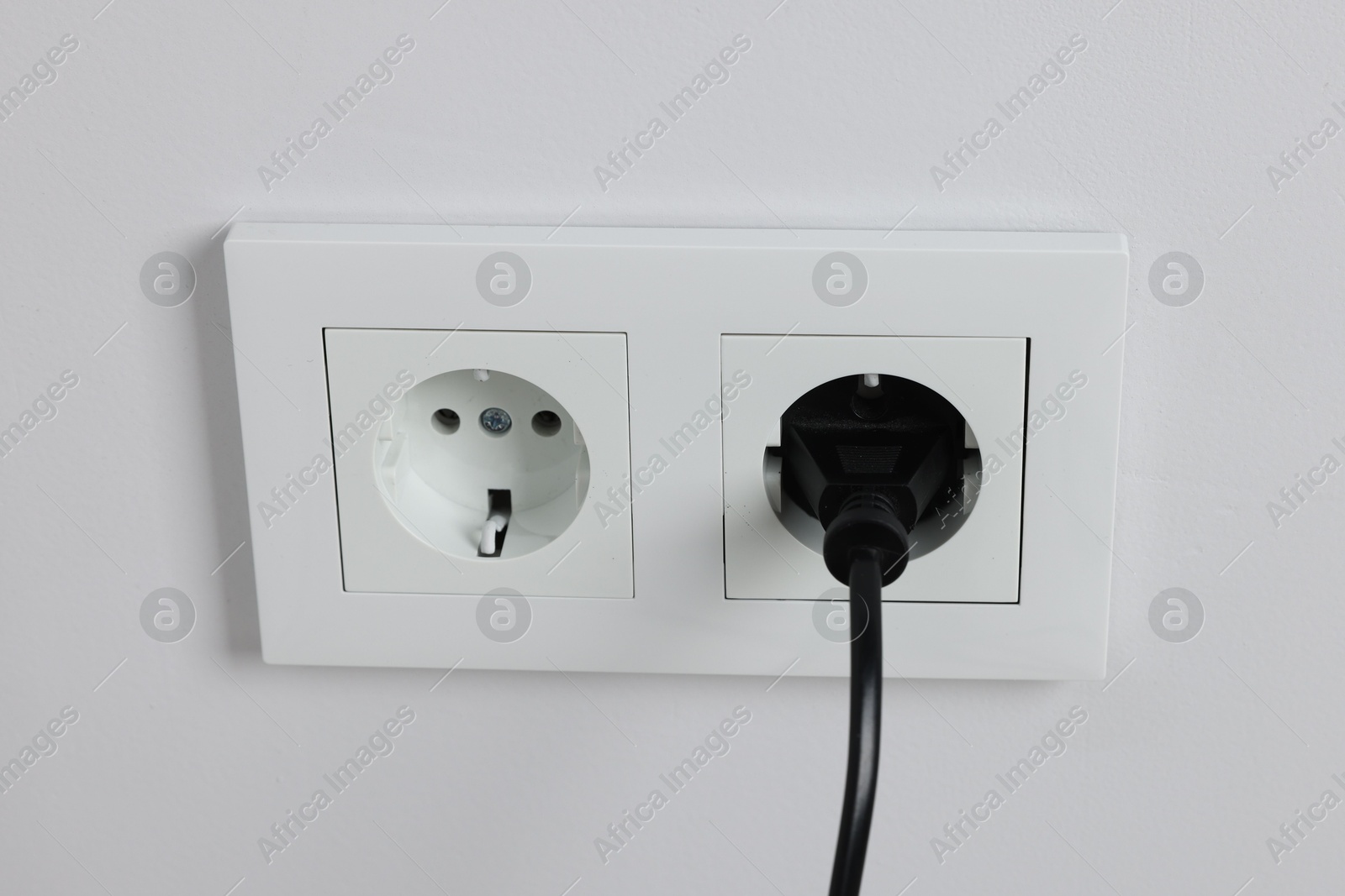 Photo of Power plug in socket on white wall, closeup