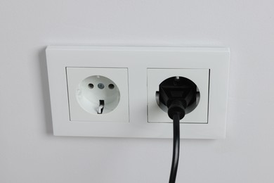 Photo of Power plug in socket on white wall, closeup