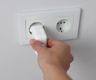 Photo of Man plugging USB adapter into power socket on white wall, closeup