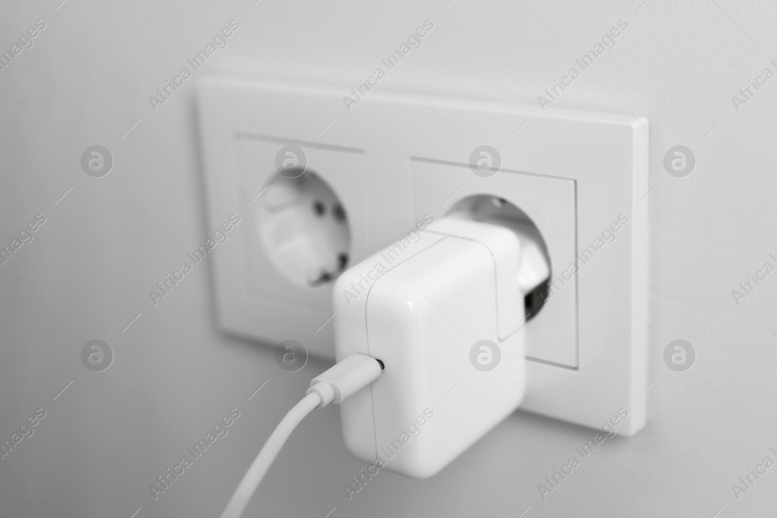 Photo of USB adapter with cable in power socket on white wall, closeup