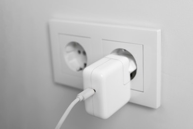 Photo of USB adapter with cable in power socket on white wall, closeup
