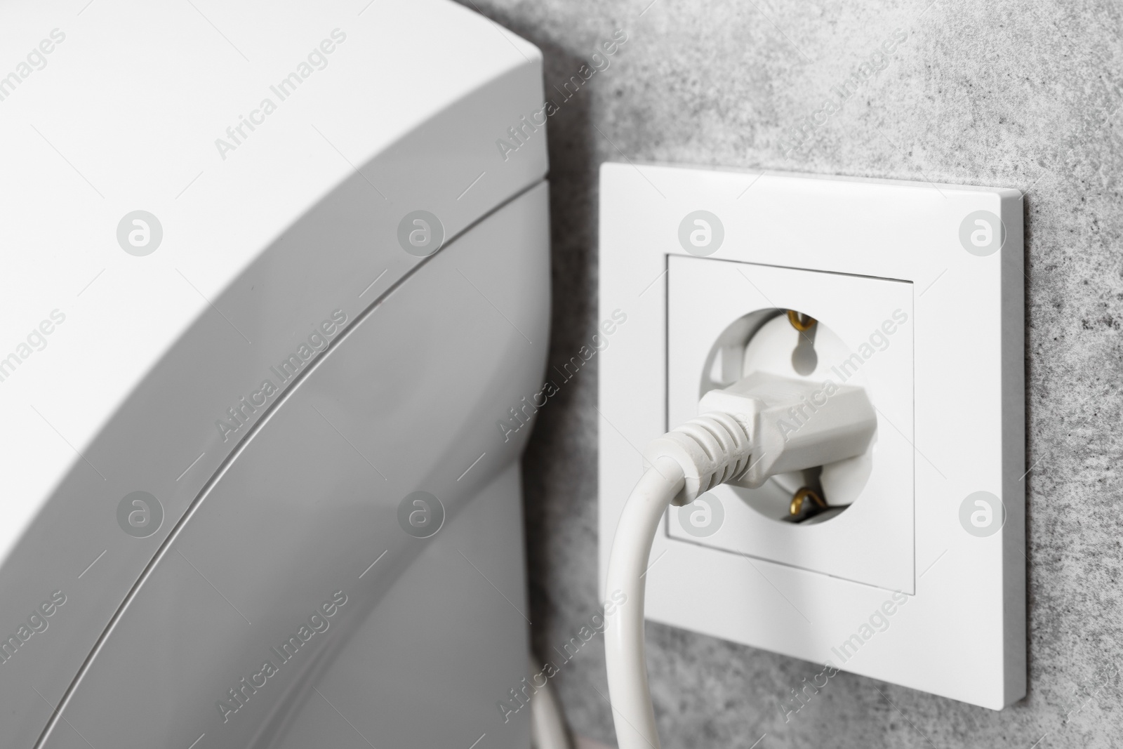 Photo of Power plug in socket on grey wall, closeup