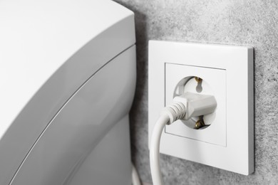 Photo of Power plug in socket on grey wall, closeup