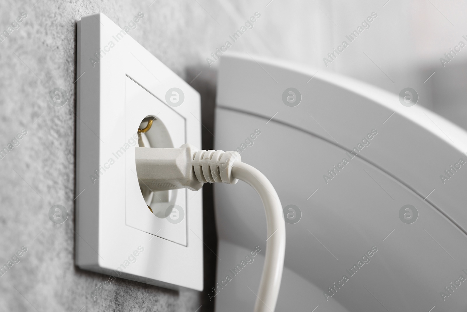 Photo of Power plug in socket on grey wall, closeup