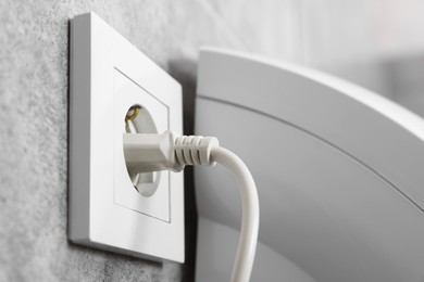 Photo of Power plug in socket on grey wall, closeup