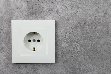 Photo of Electric power socket on grey wall, space for text