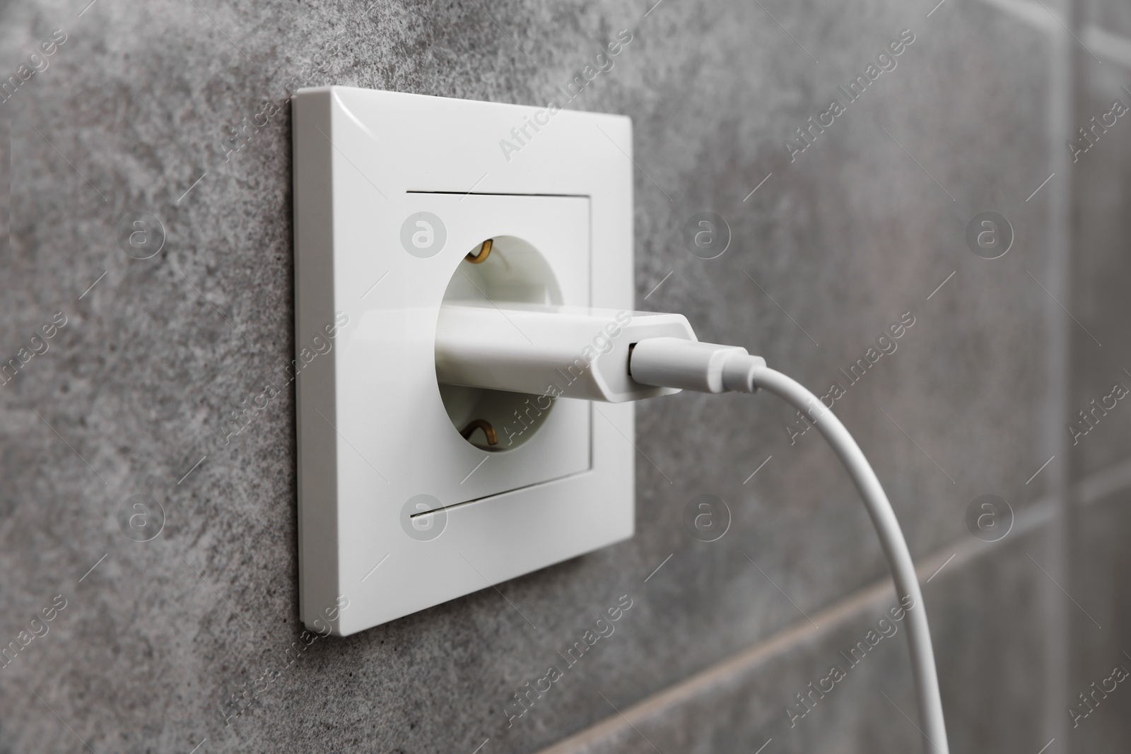 Photo of USB adapter with cable plugged into electric socket on grey wall, closeup