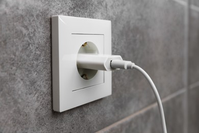 Photo of USB adapter with cable plugged into electric socket on grey wall, closeup