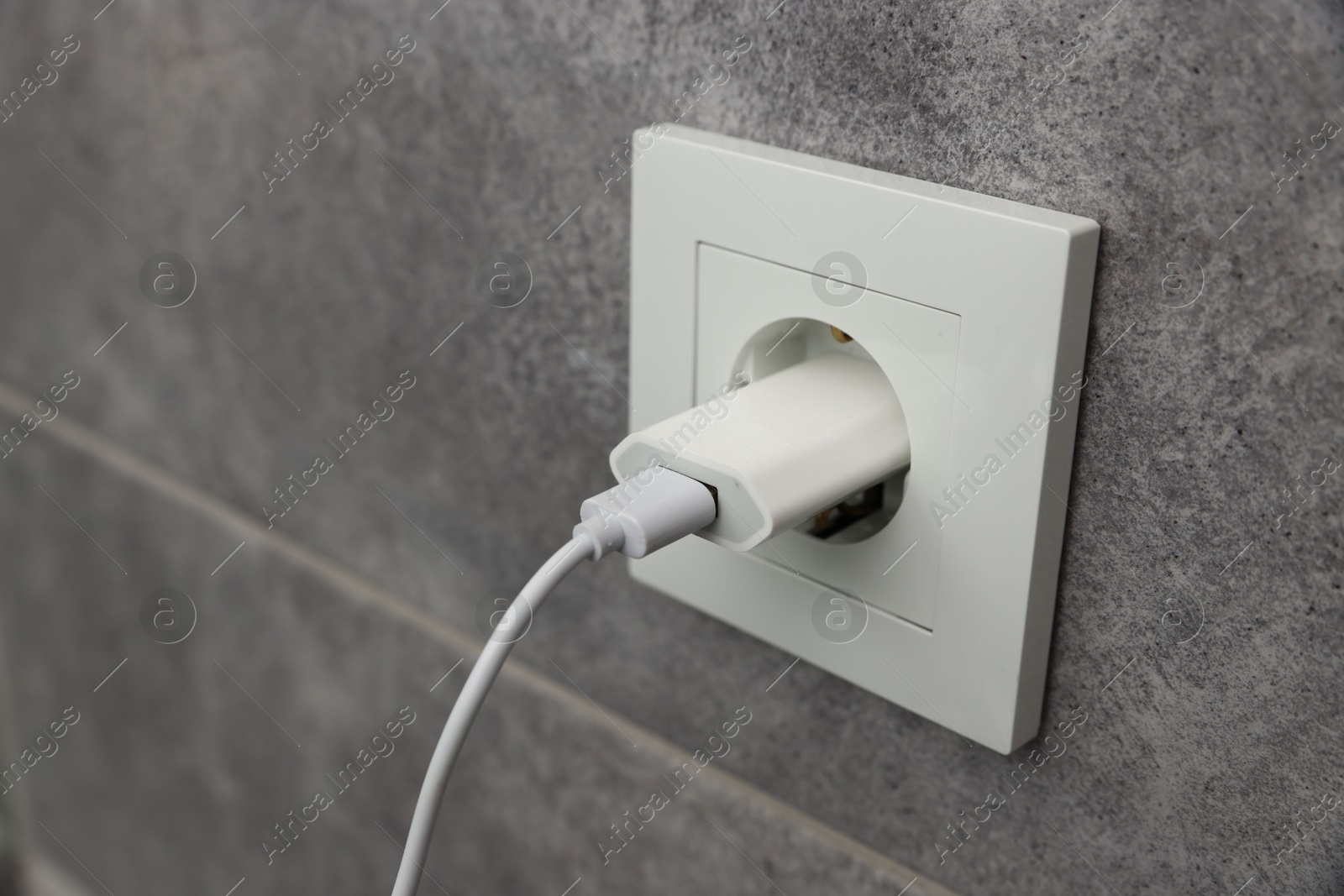 Photo of USB adapter with cable plugged into electric socket on grey wall, closeup. Space for text