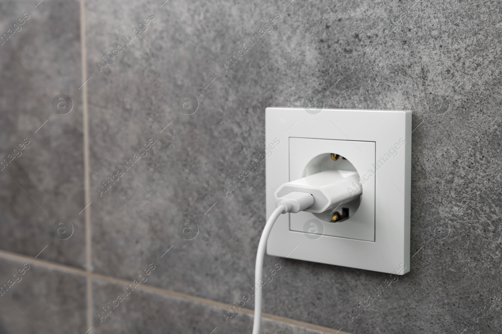Photo of USB adapter with cable plugged into electric socket on grey wall, closeup. Space for text