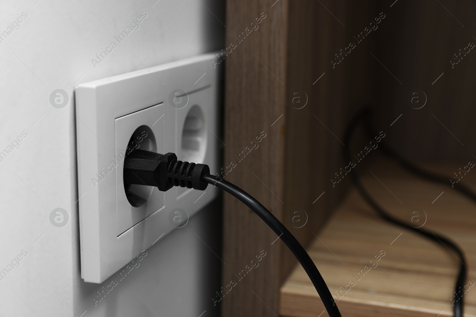 Photo of Power socket with electric plug on white wall, closeup