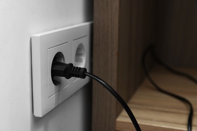 Photo of Power socket with electric plug on white wall, closeup
