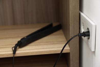Photo of Hair straightener plugged into power socket indoors, closeup