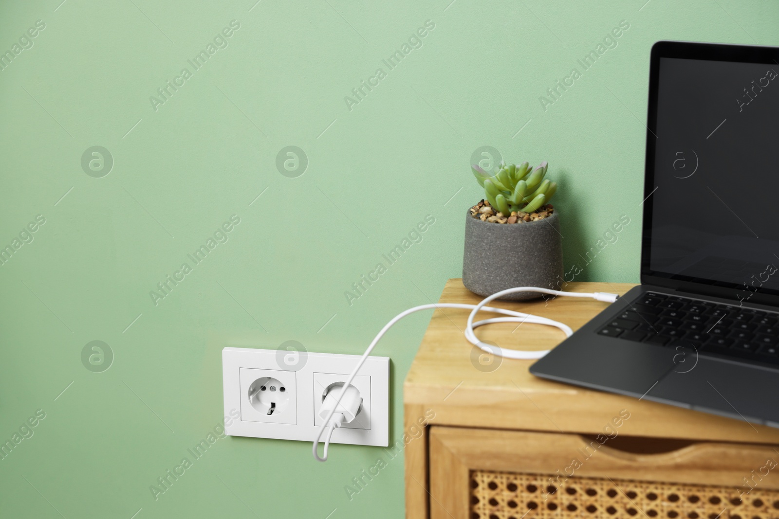 Photo of USB adapter with cable plugged into electric socket charging laptop indoors