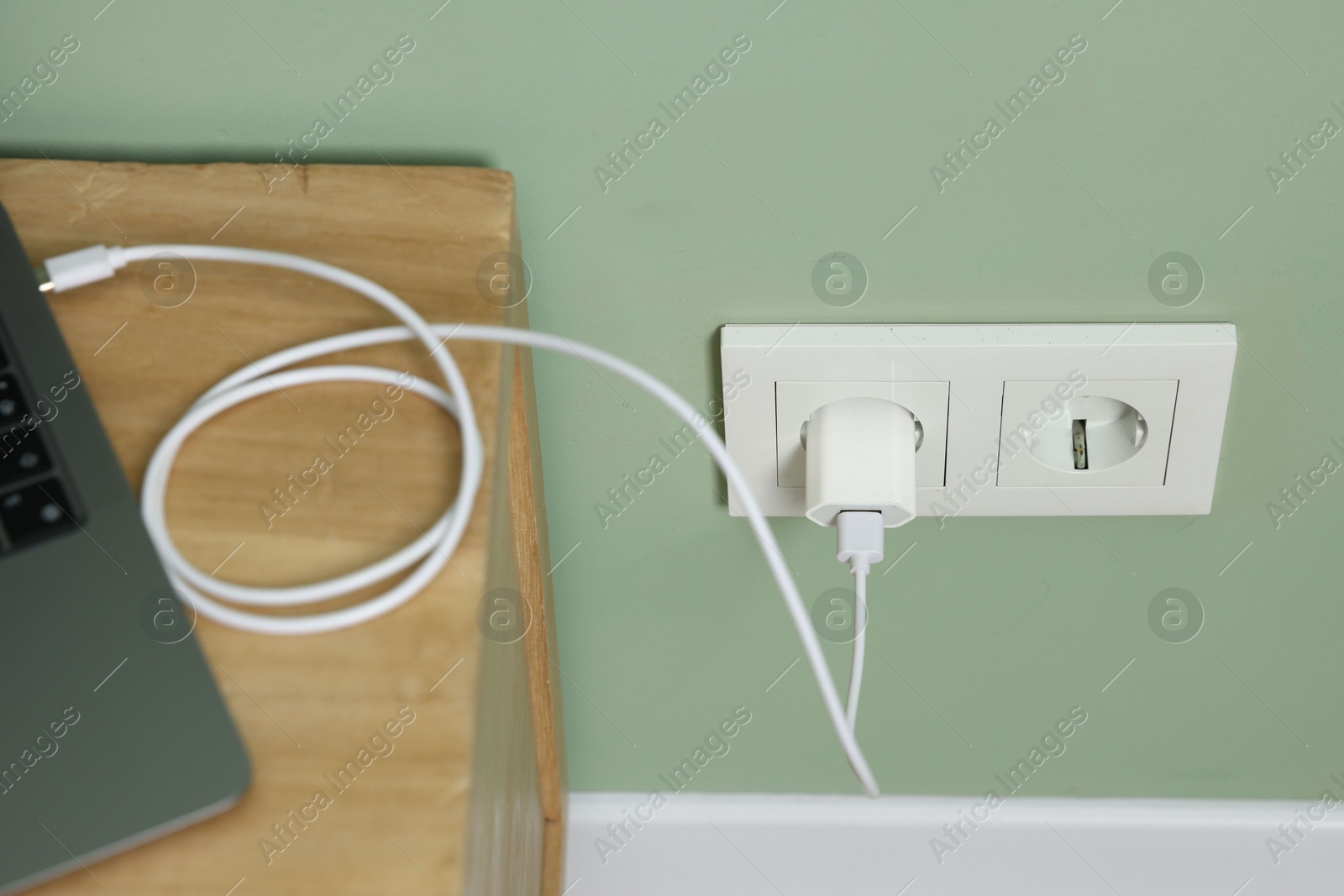 Photo of USB adapter with cable plugged into electric socket charging laptop indoors, above view