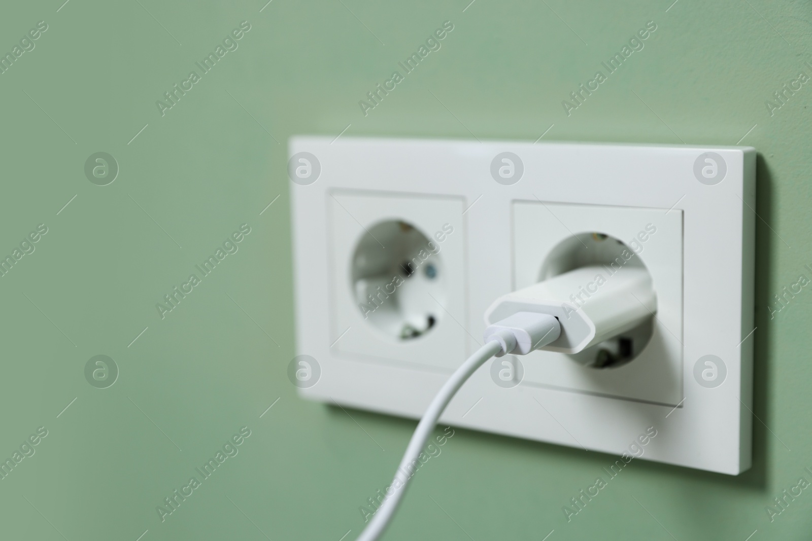 Photo of USB adapter with cable plugged into electric socket on green wall, closeup. Space for text