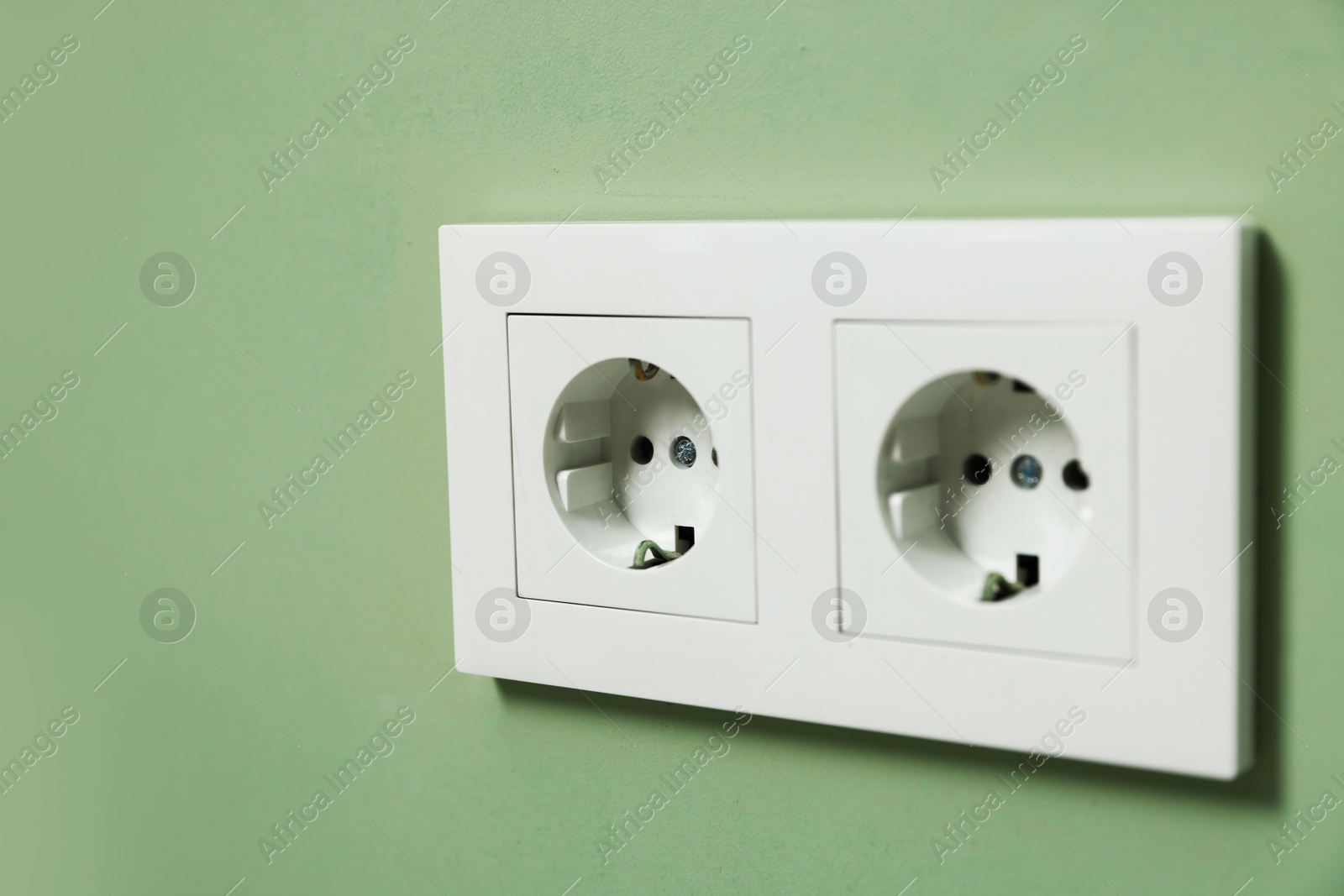 Photo of Electric power sockets on green wall, closeup. Space for text