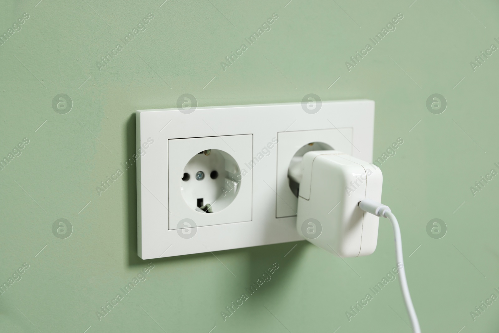 Photo of USB adapter with cable plugged into electric socket on green wall, closeup