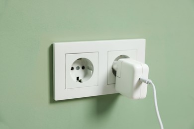 Photo of USB adapter with cable plugged into electric socket on green wall, closeup