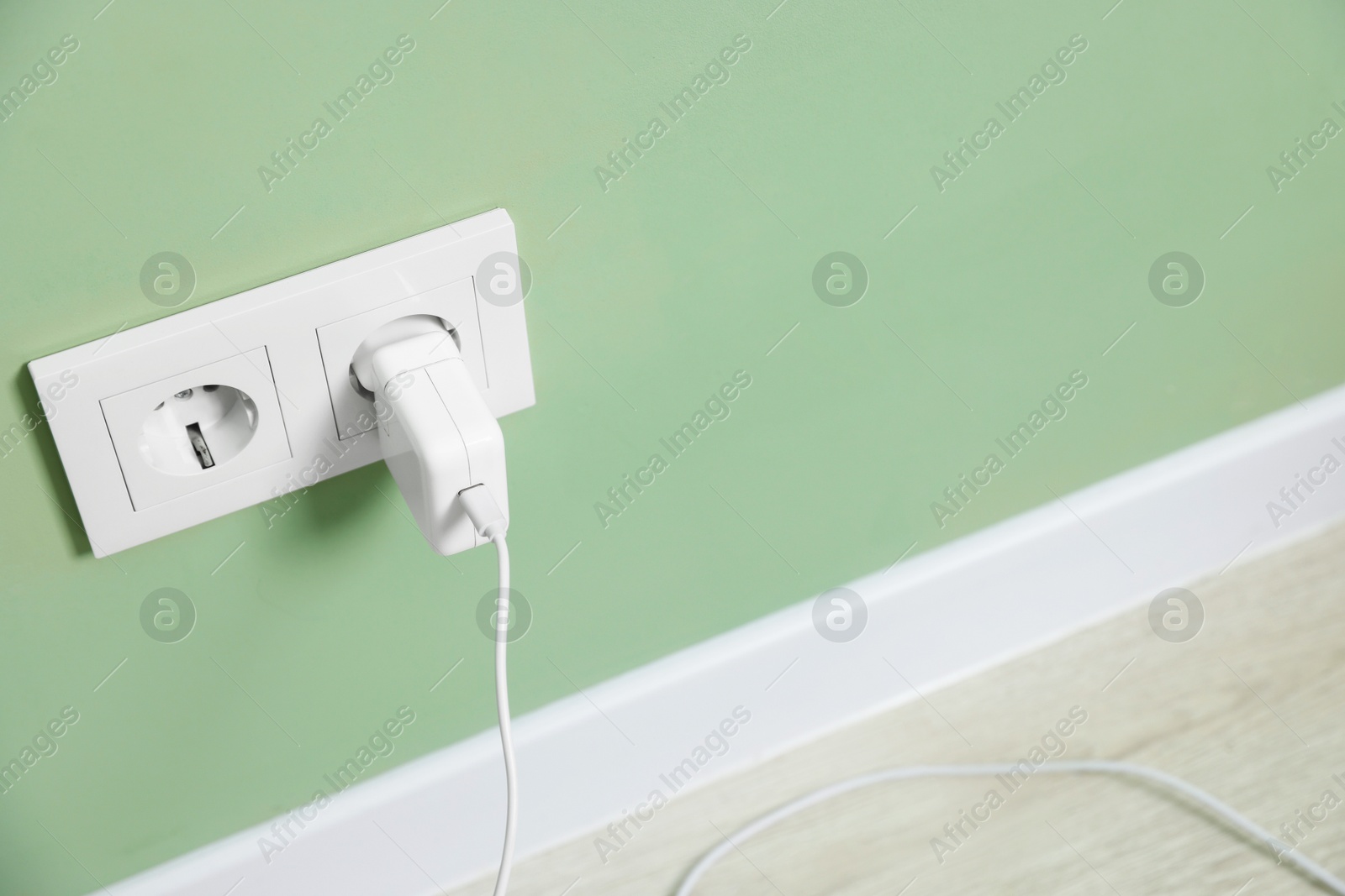 Photo of USB adapter with cable plugged into electric socket on green wall, space for text