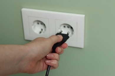 Photo of Woman inserting electric plug into power socket on green wall, closeup